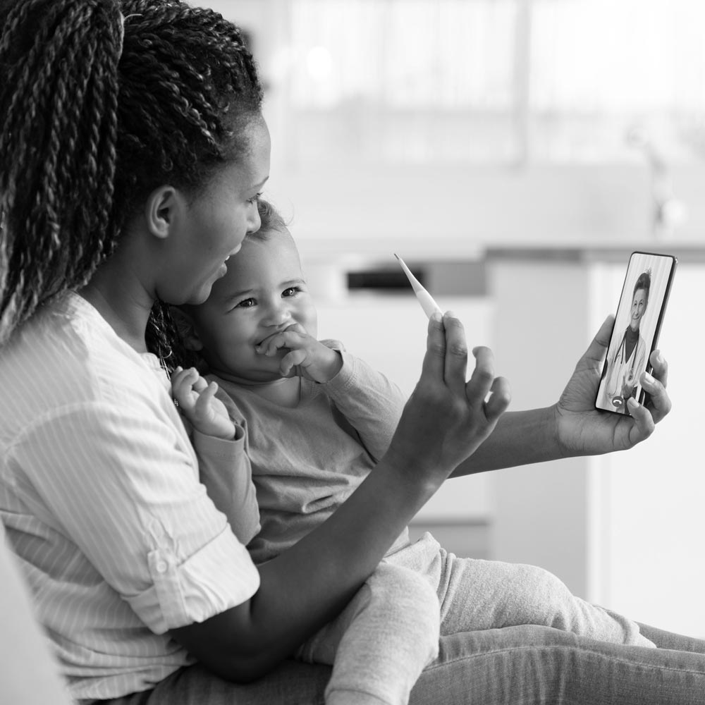 A woman and her child reading a thermometer and discussing results with a doctor on a mobile device.